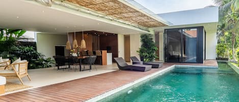 A modern outdoor pool area with a wooden deck, lounge chairs, and a dining setup.