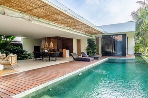 A modern outdoor pool area with a wooden deck, lounge chairs, and a dining setup.