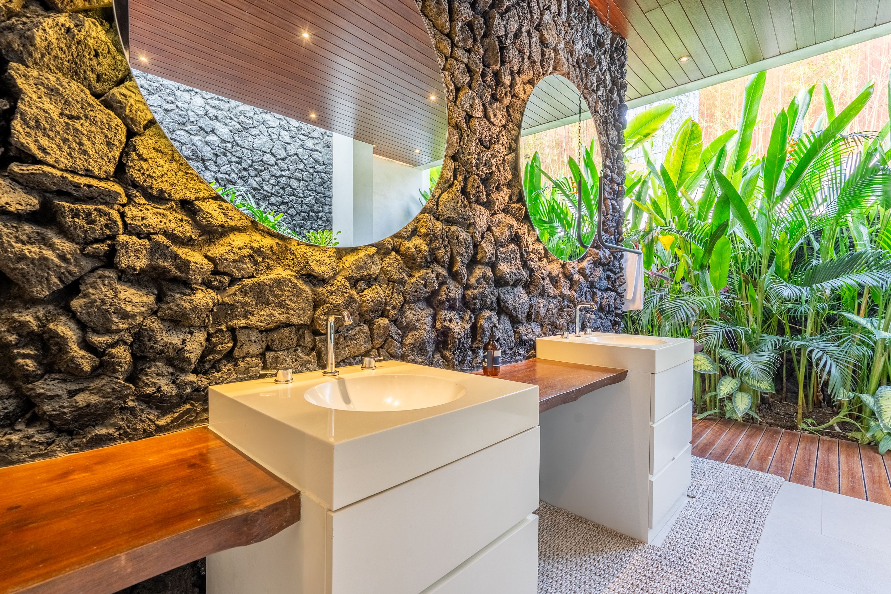 A bathroom with a stone wall, two sinks, and a mirror.