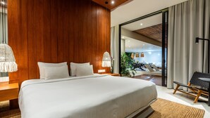 A modern bedroom with a large bed, wooden panel walls, a view of the outdoors, and a seating area with a chair and table. - Amazing 3BR Green Flow Villa in Ubud with Pool (Kec. Ubud)
