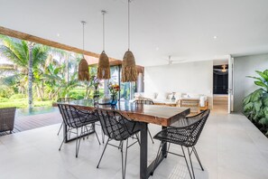 A modern dining area with a wooden table and black woven chairs, overlooking a lush garden and a pool. - Amazing 3BR Green Flow Villa in Ubud with Pool (Kec. Ubud)