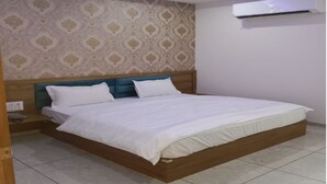 A neatly made bed with white linens, a wooden headboard, and a patterned wallpaper.