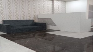 A reception area with a dark grey sofa, a white reception desk, patterned wallpaper, and a tiled floor with a mix of dark and light tiles.