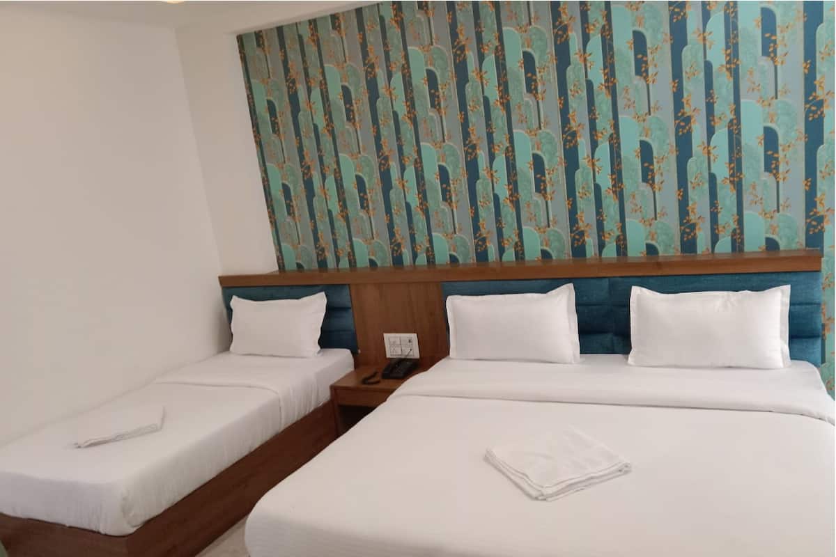 Una camera d'albergo con due letti singoli e un letto matrimoniale più grande, tutti con lenzuola bianche.