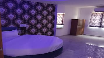 Una habitación de hotel con una cama grande, papel tapiz estampado, un armario y una ventana con cortinas.