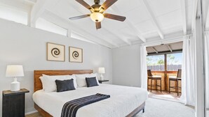 Amplia habitación con una cama grande, dos mesitas de noche con lámparas, ventilador de techo y vista a un patio exterior.