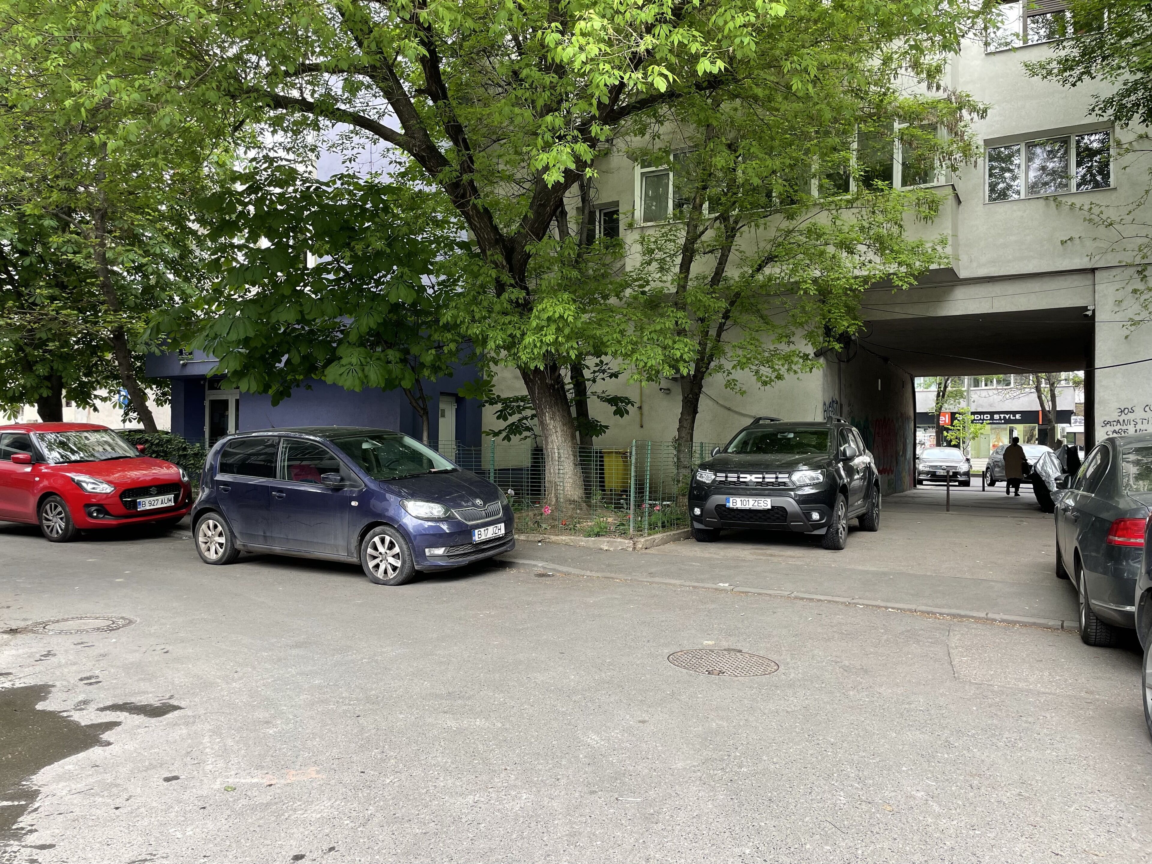 En gatubild med parkerade bilar, träd och en byggnad med en skylt som visar texten "el Audio Style".