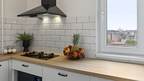 Une cuisine moderne avec des carreaux blancs, une cuisinière à gaz, une hotte noire et une fenêtre donnant sur la ville.