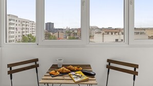 Une pièce avec une table en bois mise pour le petit-déjeuner, deux chaises et une vue sur la ville grâce à de grandes fenêtres.