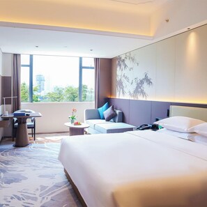 A hotel room with a large bed, a desk, a chair, a sofa, and a view of the city through the window. - Guangdong Yingbin Hotel (Guangzhou)