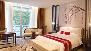 A hotel room with a large bed, a sofa, a desk, and a view of greenery through the window. - Guangdong Yingbin Hotel (Guangzhou)