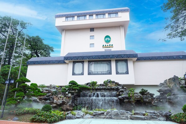 A hotel building with a traditional architectural style, a waterfall feature in front, and a clear sky in the background. - Guangdong Yingbin Hotel (Guangzhou)