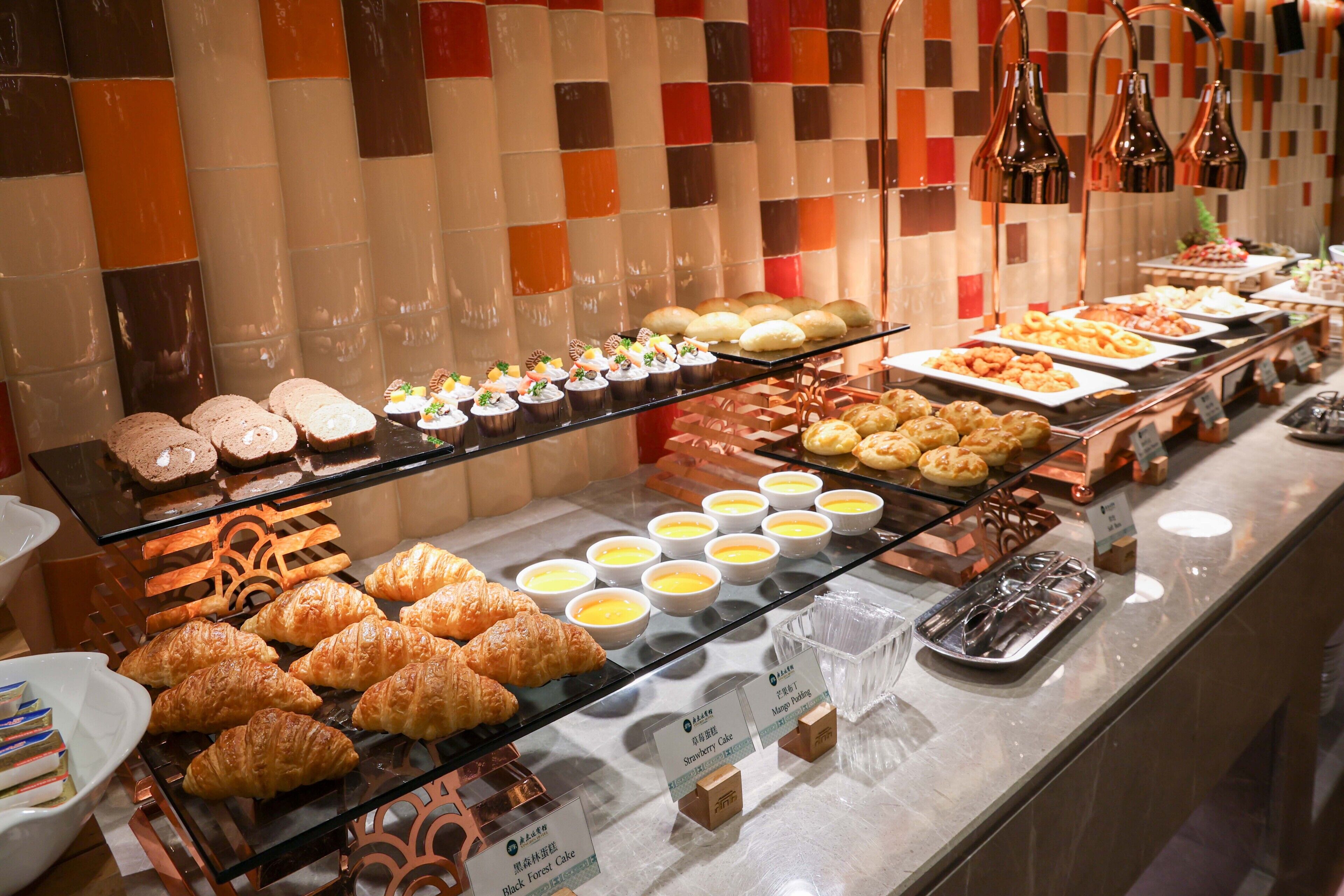 Buffet com diversos itens de comida, incluindo doces, sobremesas e uma seleção de pães.