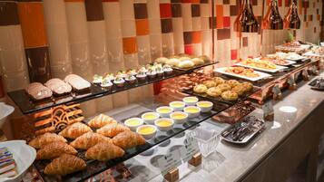 Buffet com diversos itens de comida, incluindo doces, sobremesas e uma seleção de pães.