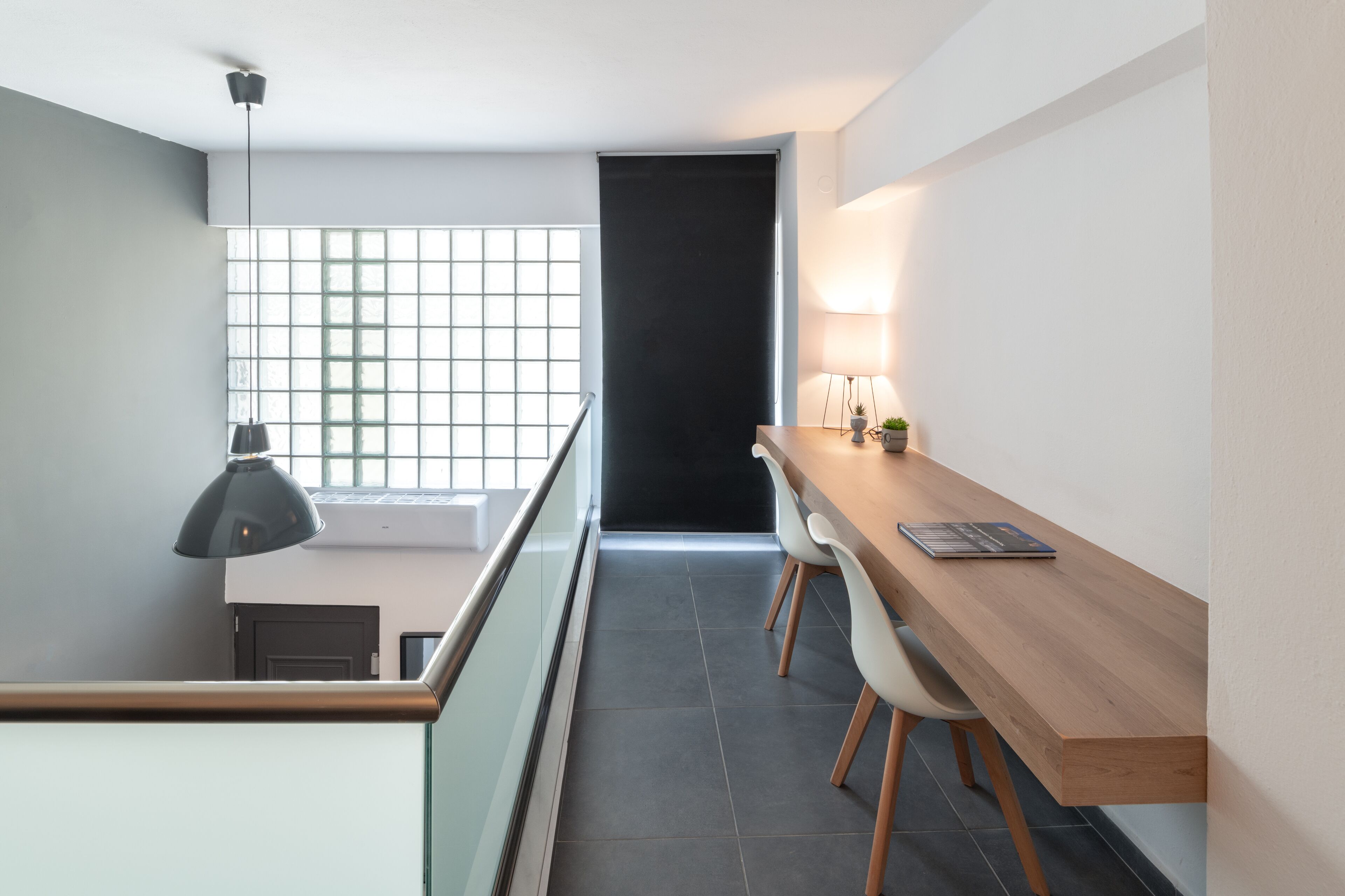Una habitación moderna y minimalista con un escritorio de madera, dos sillas blancas, una lámpara negra y un ventanal con diseño de cuadrícula.