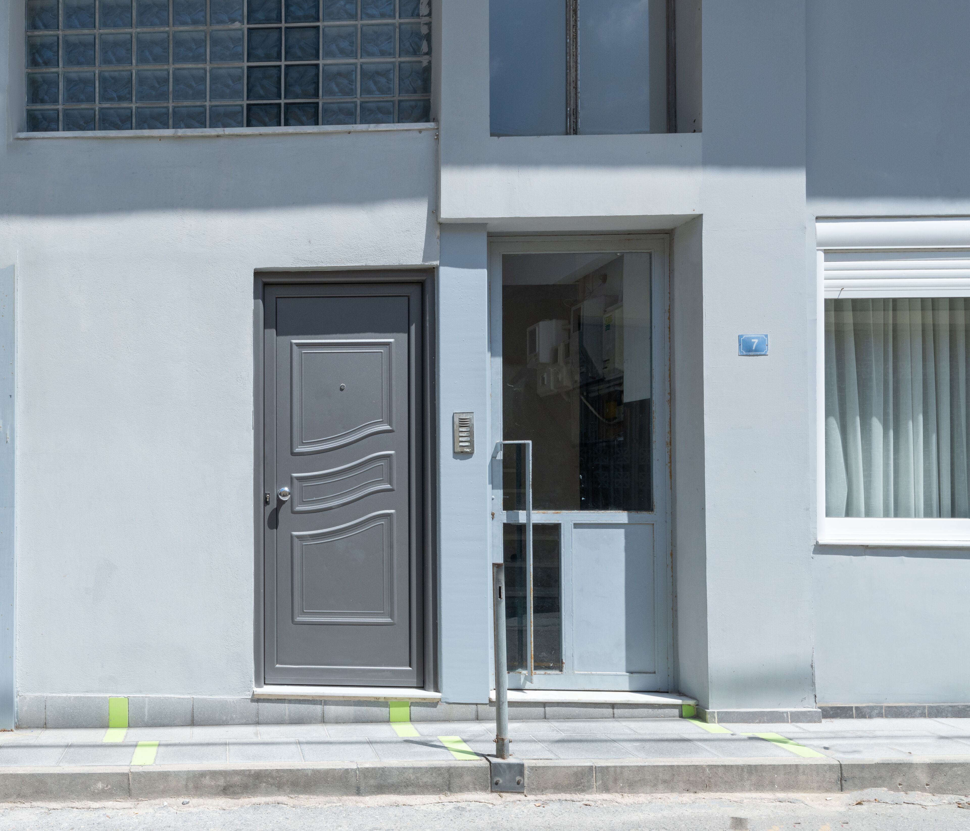Un edificio con una puerta gris, un ventanal pequeño y un letrero con el número 7.