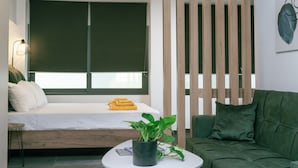 A modern room with a bed, a green sofa, a small table with a plant, and a wall-mounted lamp. - Zen Central Luxury Apartment (Heraklion)