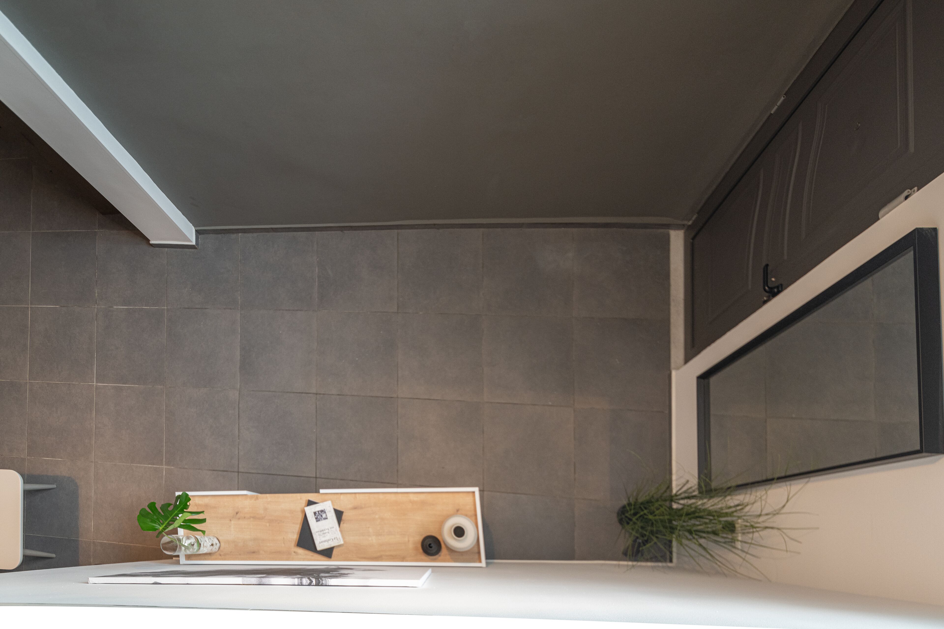 A modern kitchen with grey tiles, a wooden countertop, and a window.