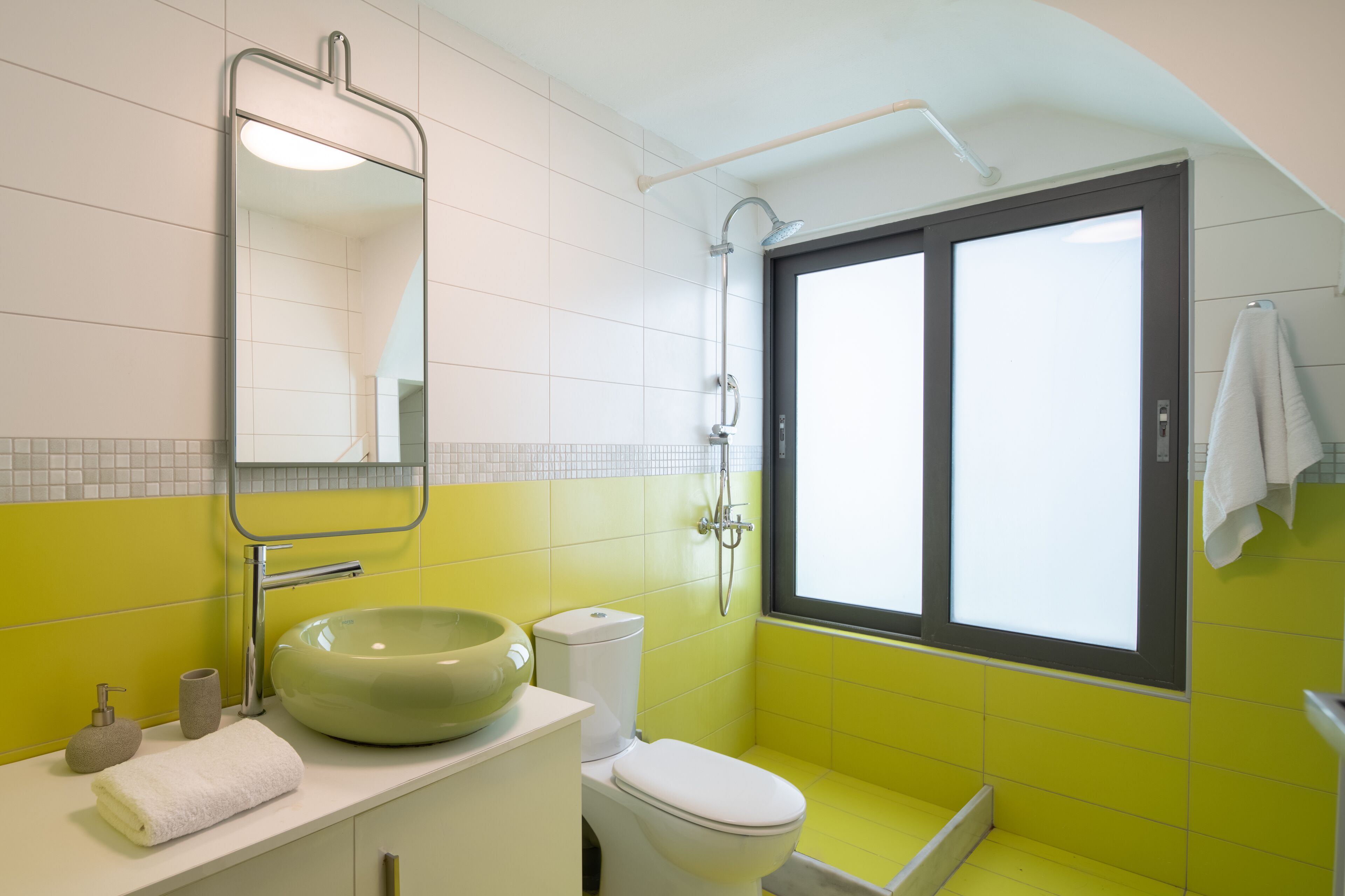 A bathroom with a green sink, white toilet, and a window with a towel hanging on the right.
