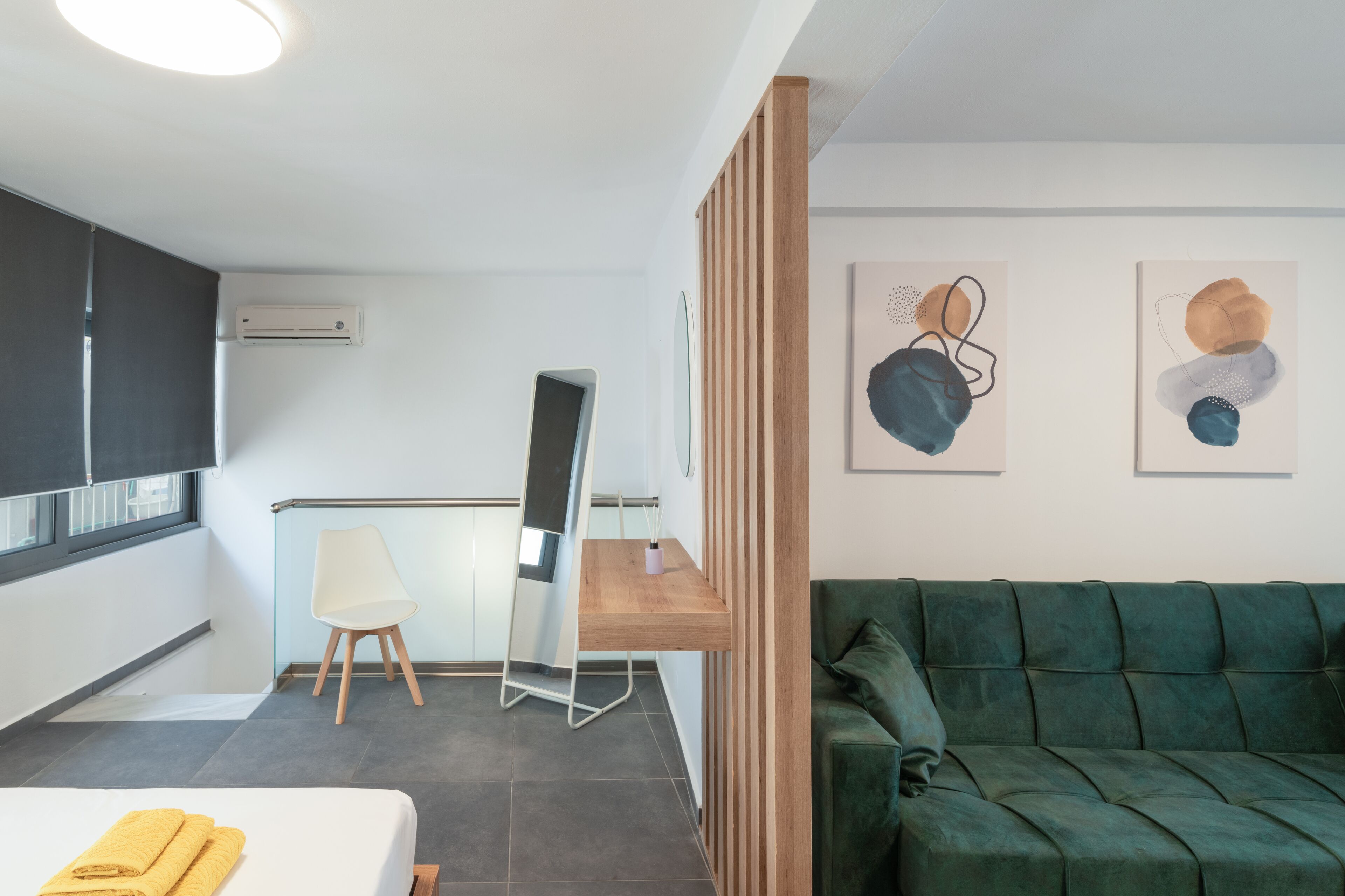 Une chambre d’hôtel moderne avec un lit, un bureau, un canapé vert et des œuvres d’art abstraites accrochées au mur.