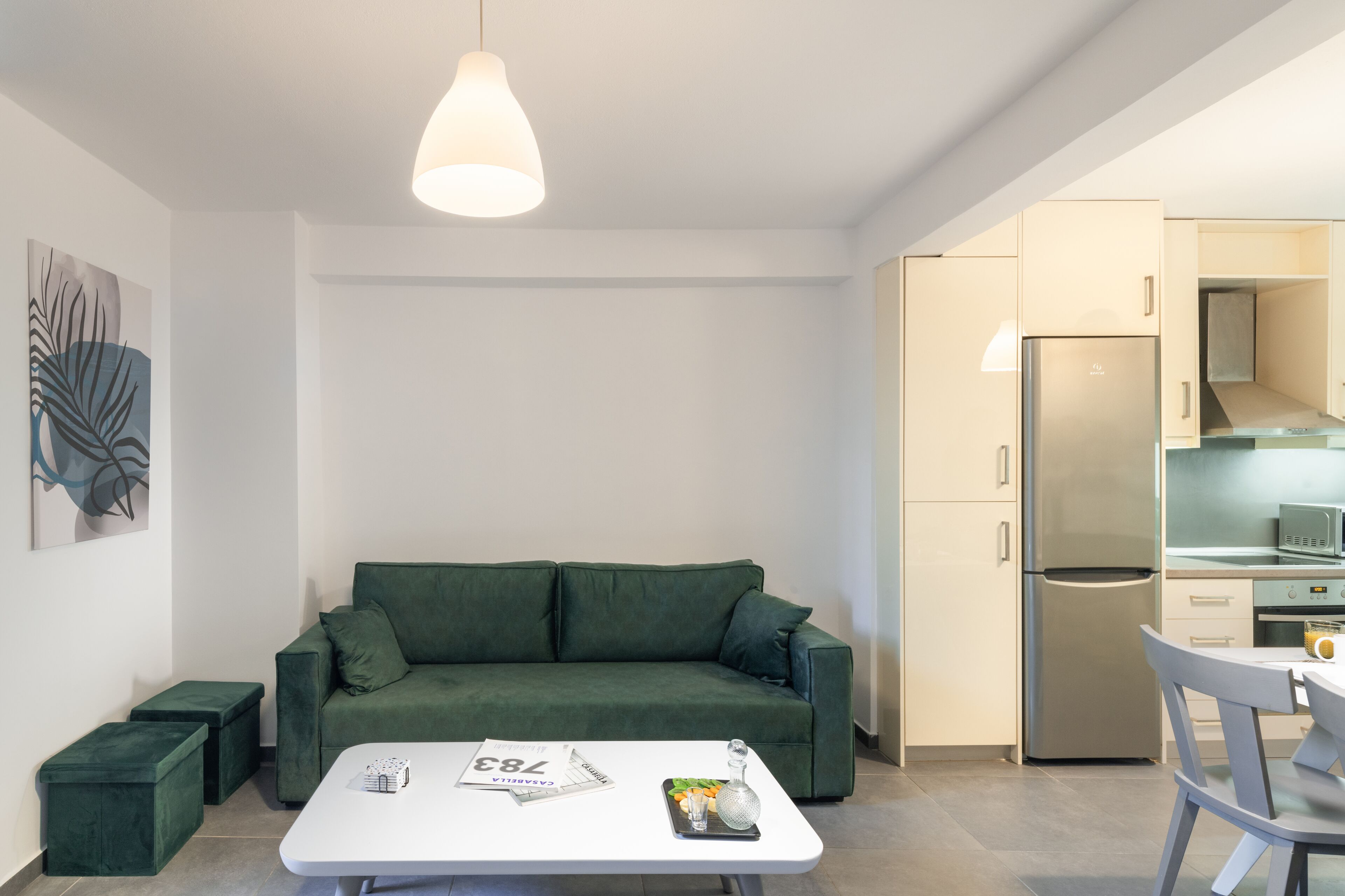 A modern kitchen with a built-in refrigerator, a dining table with chairs, and a green sofa in a living area.