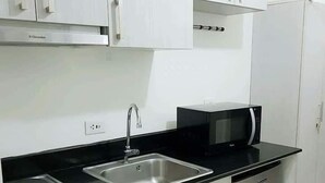 A compact kitchen with a black countertop, stainless steel sink, microwave, stove, and a dishwasher. - Green Residences  Taft (Manila)