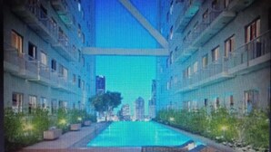 A modern hotel with a central pool, multiple floors, and a cityscape view. - Green Residences  Taft (Manila)