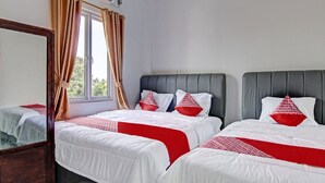 Ein Hotelzimmer mit zwei Betten, jeweils mit weißer Bettwäsche und roten Akzenten, einem großen Spiegel und einem Fenster mit Vorhängen.