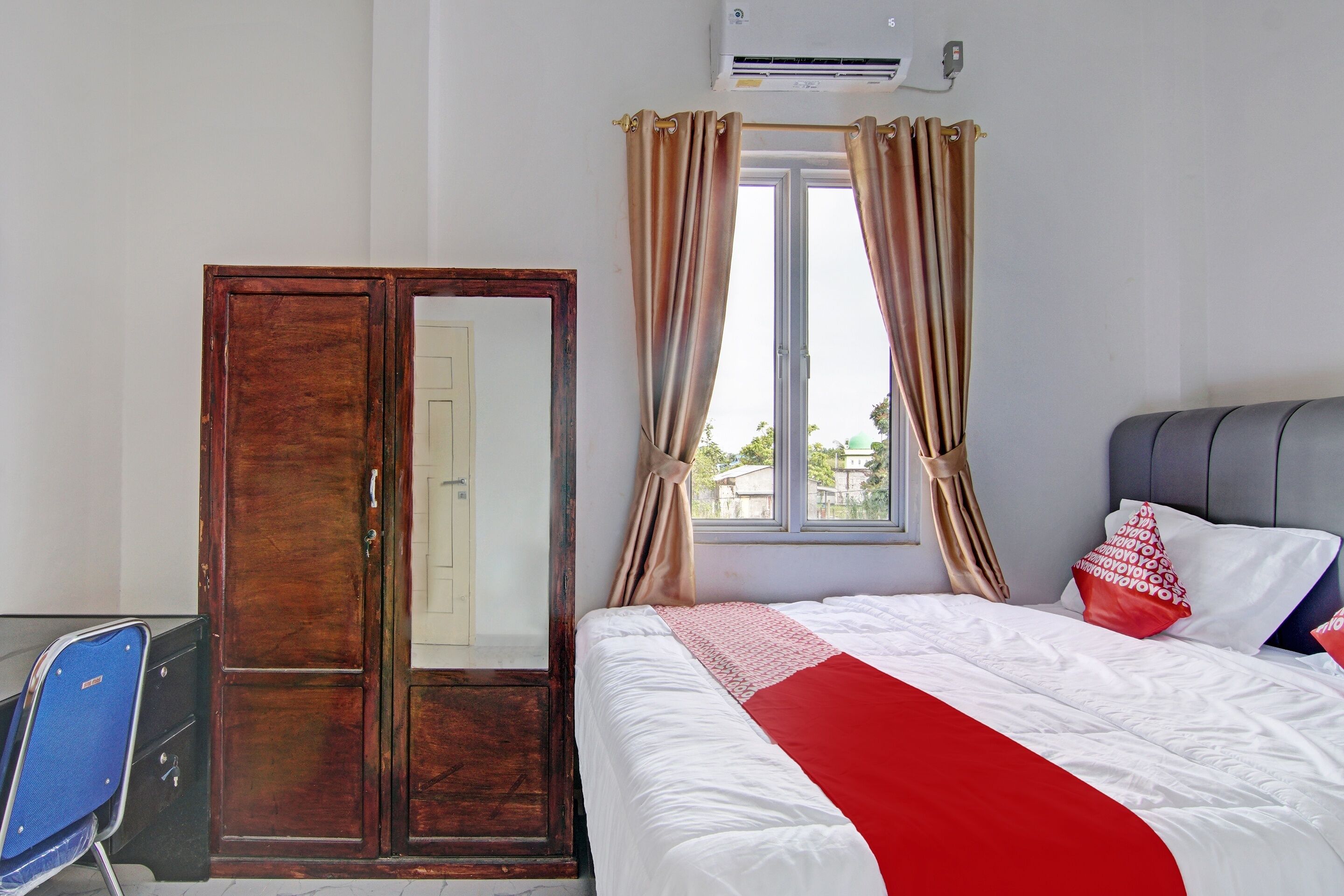 A bedroom with a bed, a wardrobe, a window with curtains, and an air conditioning unit.