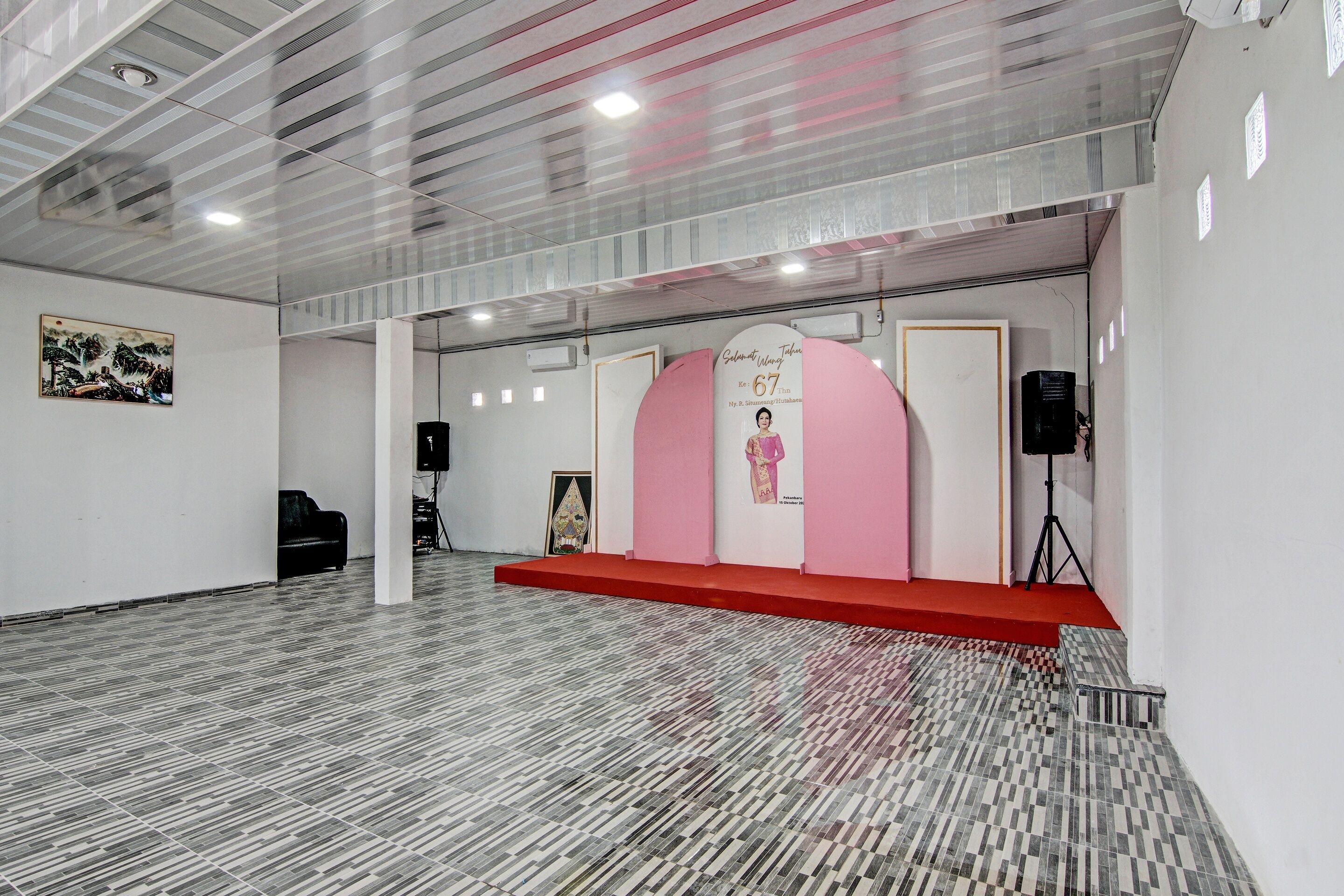 Une pièce spacieuse avec un sol à motifs, une scène recouverte d’un tapis rouge et un tableau encadré accroché au mur.