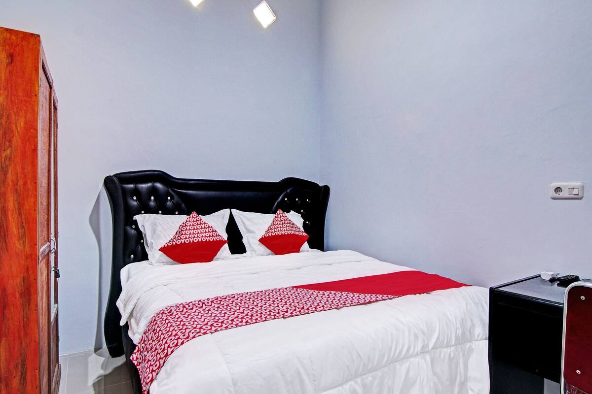 A neatly made bed with a black headboard, white bedding, and red and white patterned pillows.