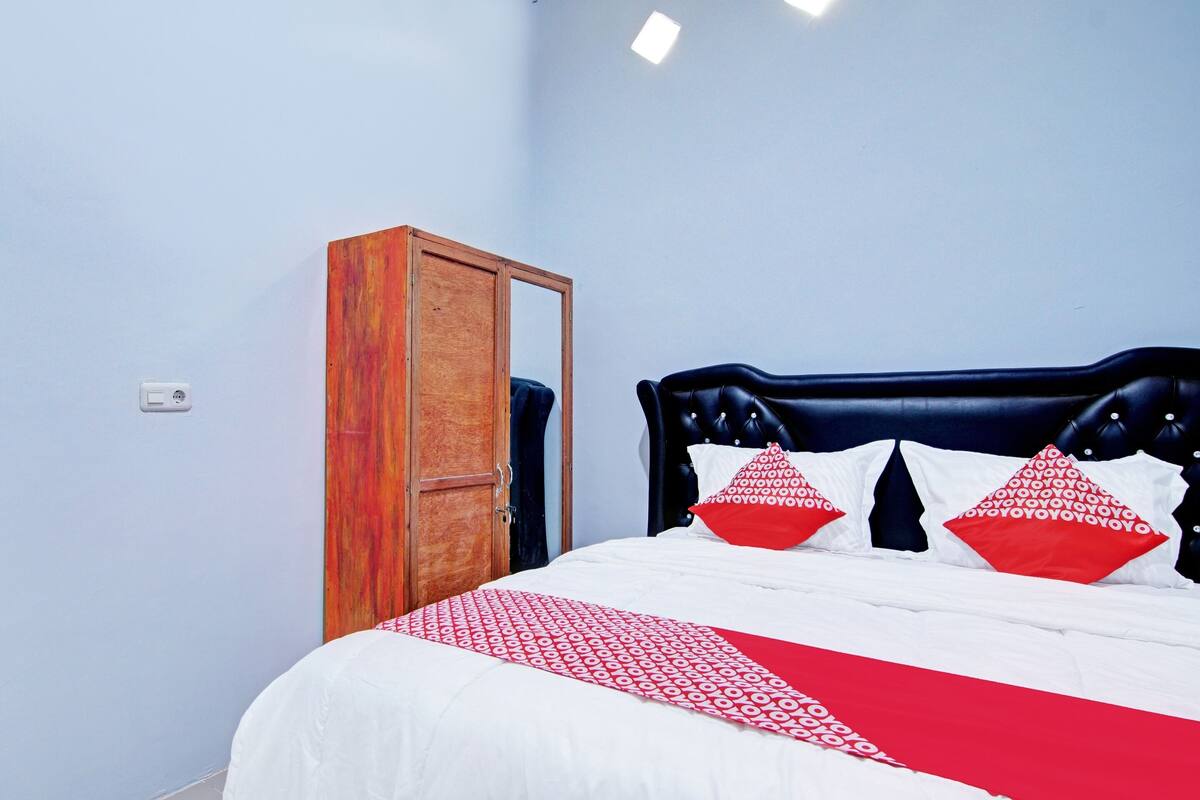 A bedroom with a bed, a wooden wardrobe, and a mirror.