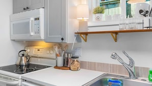Una cucina moderna con mobili bianchi, un forno a microonde, un bollitore, uno scaffale in legno con bicchieri e un lavandino in acciaio inossidabile.