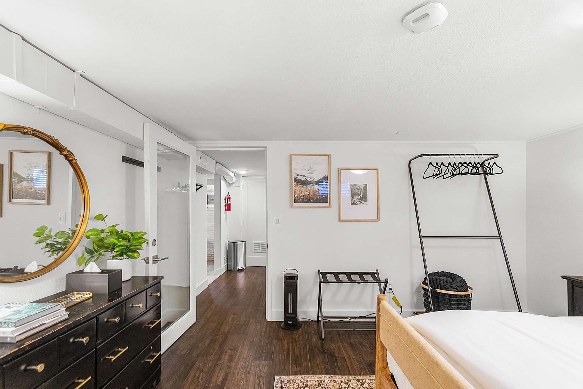 A modern bedroom with a bed, dresser, mirror, and artwork.
