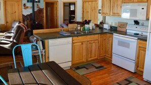 A kitchen with wooden cabinets, a white dishwasher, a stove, and a dining area with a bench and chairs. - Marr's Mountain Cabins - Cabin 1 (Red Feather Lakes)