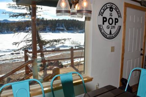 A dining area with a view of a snowy landscape, a wooden deck, and a sign that reads "PLACE OF PEACE The POP since 2019".