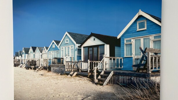 A row of beach houses with wooden decks and railings, arranged along a sandy beach.