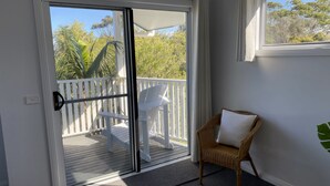 A room with a sliding glass door leading to an outdoor deck with a white chair and a wicker chair with a cushion.