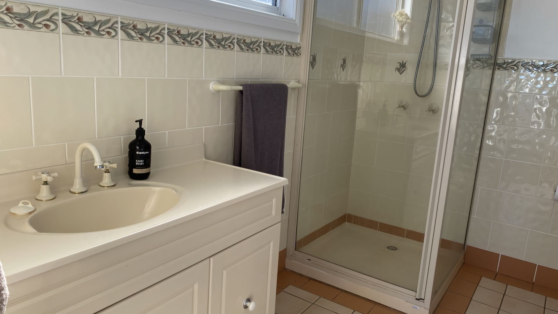 Een badkamer met een wastafel, twee kraan, een zeepdispenser en een douche met een glazen deur.
