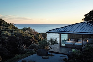 A modern house with a glass-enclosed patio overlooking a body of water. - WEAZER Nishiizu (Numazu)