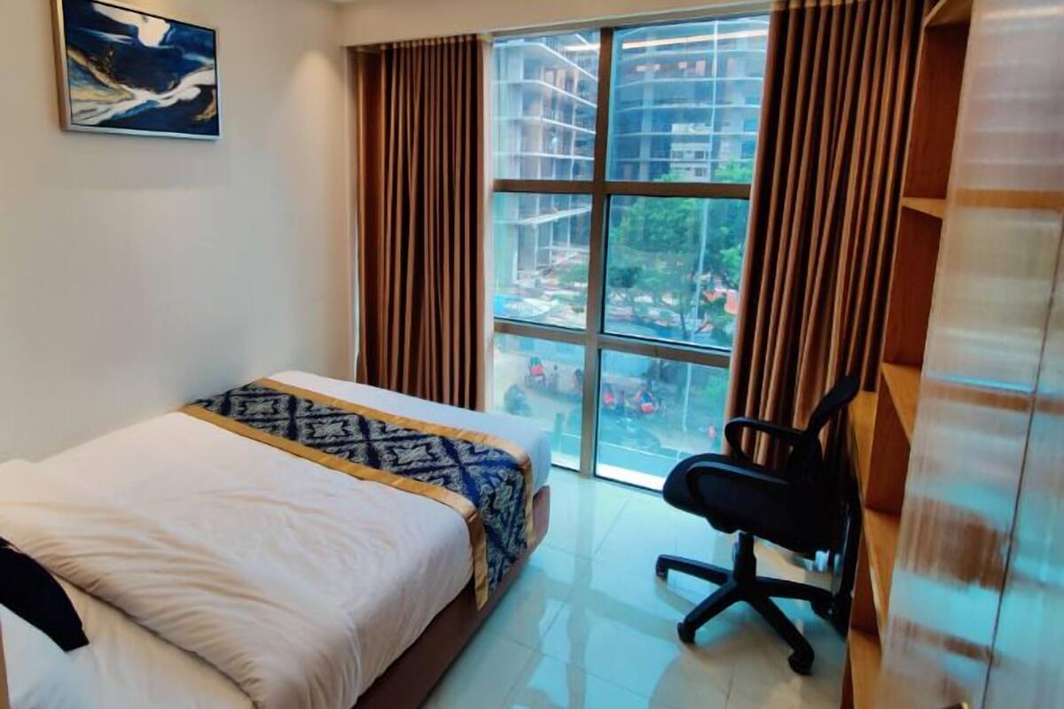 A bedroom with a bed, a desk, and a large window with curtains.