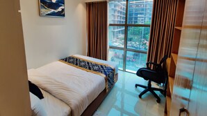 A hotel room with a bed, a desk, a chair, a window with curtains, and a painting on the wall. - Hotel Royal Bengal (Dhaka)