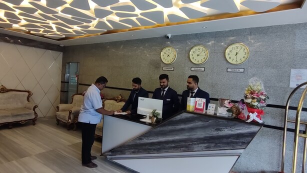 A reception area with a modern design, featuring a reception desk, three clocks indicating different time zones, and a decorative wall. - Hotel Royal Bengal (Dhaka)