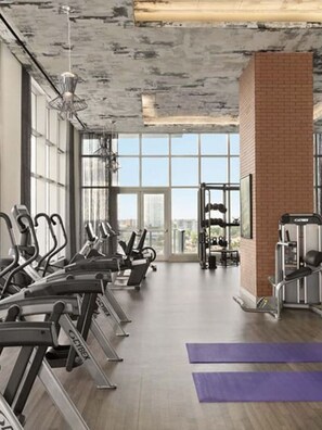 Ein Fitnessstudio mit Laufbändern, Kraftgeräten und einem großen Fenster mit Blick auf die Stadt.