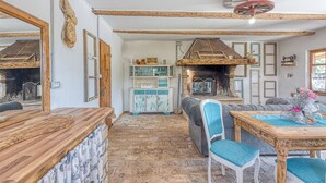 Un interior rústico con vigas de madera a la vista, una chimenea de piedra y una mesa de comedor de madera con sillas.