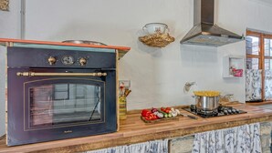 Una cocina con horno, estufa y varios vegetales sobre la encimera.