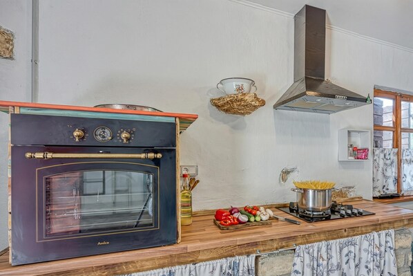 A kitchen with an oven, a stove, and various vegetables on the counter.