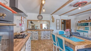 Una cocina con encimera de madera, cocina a gas y comedor con mesa de madera y sillas azules.