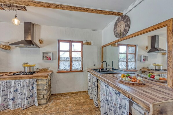 Une cuisine dotée d’un plan de travail en pierre, de poutres en bois, d’une cuisinière à gaz, d’un évier et d’un grand miroir.