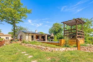 A rustic outdoor setting with a stone wall, a wooden pergola, and a house with a chimney. - Rustic Home Izabel With Pool (Pazin)